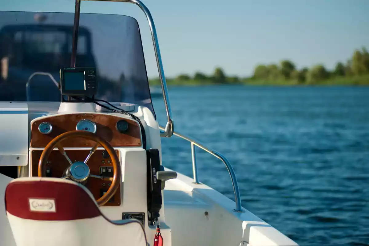 Un bote con un volante de madera y un panel de control en el agua, con un paisaje de árboles al fondo.