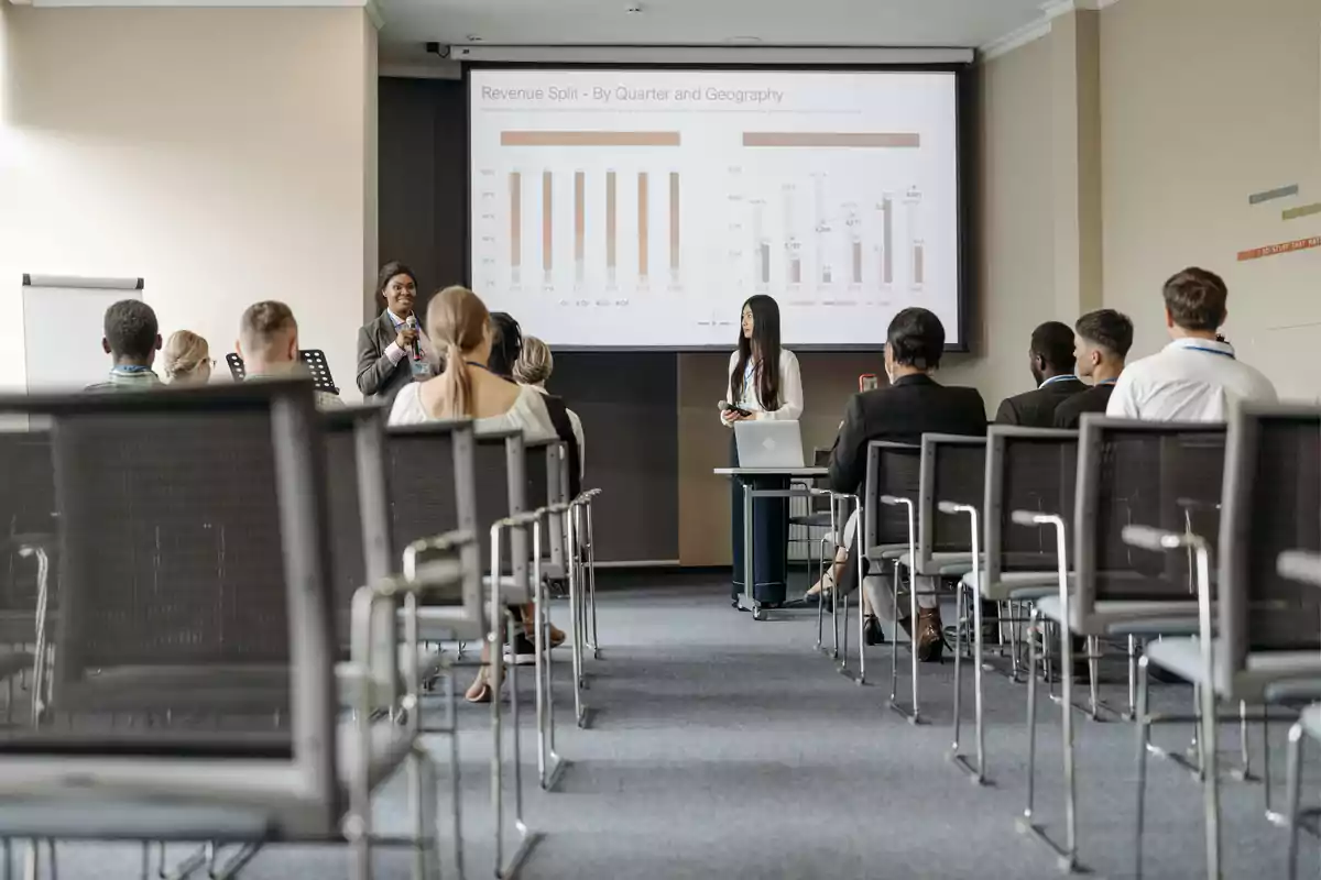 Personas asistiendo a una presentación en una sala de conferencias con gráficos proyectados en una pantalla.