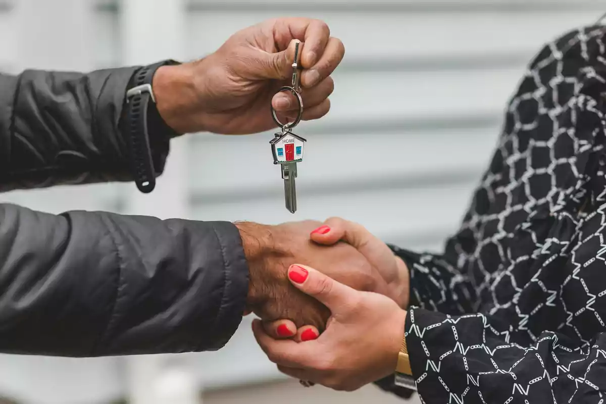 Dos personas estrechándose la mano mientras una de ellas sostiene una llave con un llavero en forma de casa.