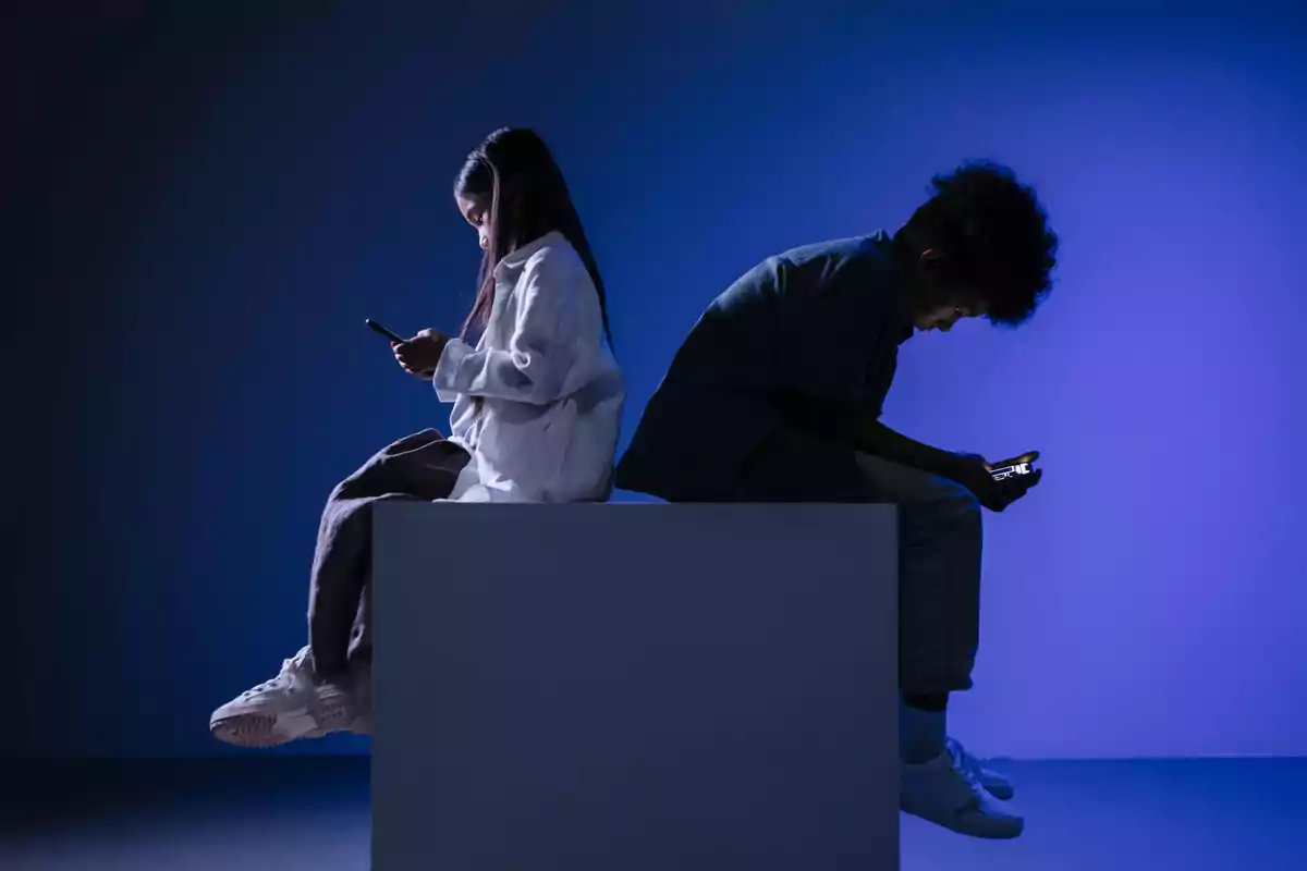 Dos personas sentadas de espaldas usando teléfonos móviles en un ambiente con iluminación azul.