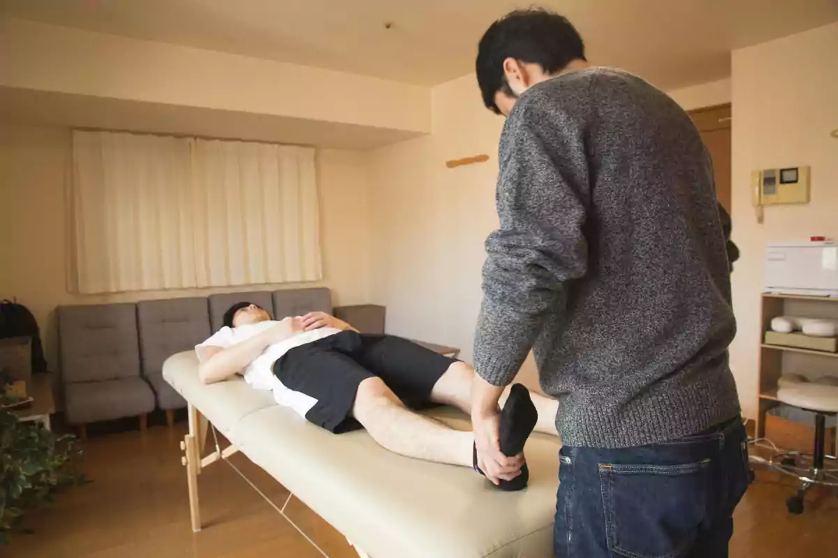 Persona recibiendo terapia física en una camilla mientras otra persona sostiene su pie en una sala acogedora
