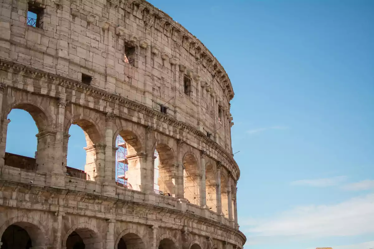 Vista lateral del Coliseo de Roma con un cielo azul claro de fondo.