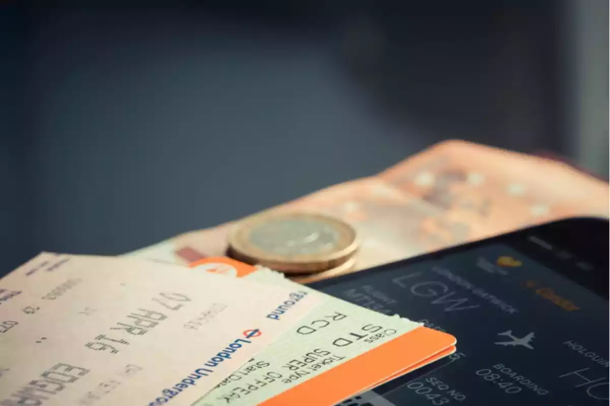 Boletos de viaje, monedas y un teléfono móvil sobre una superficie