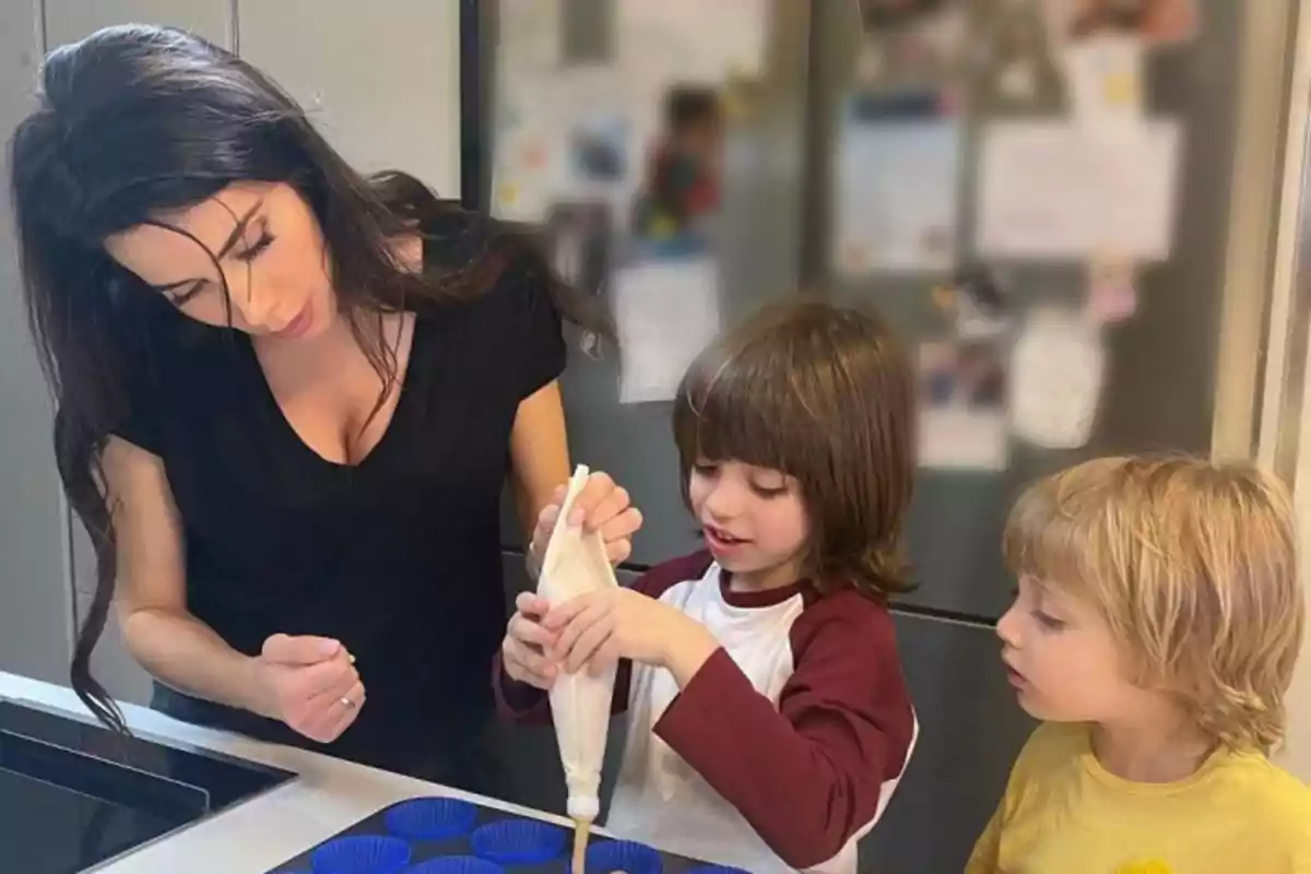 Una mujer y dos niños están en la cocina preparando algo con moldes para hornear.