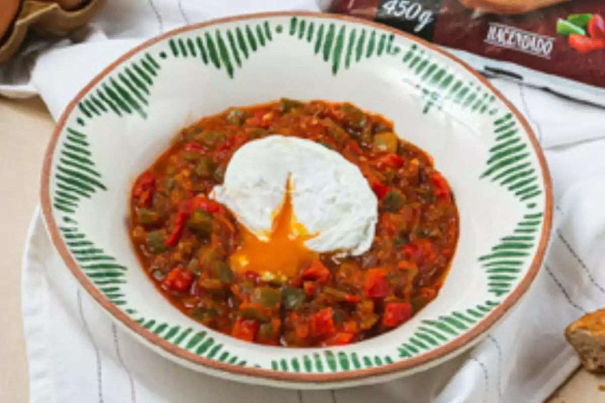 Un plato de pisto con un huevo escalfado en el centro, servido en un cuenco decorado con un diseño verde. Un plato de pisto con un huevo escalfado en el centro, servido en un cuenco decorado con un diseño verde.