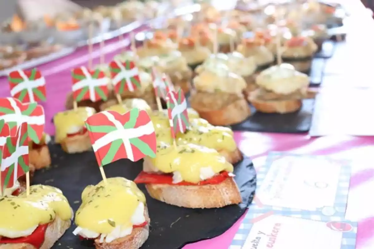 Una variedad de pintxos con banderitas vascas sobre una mesa.