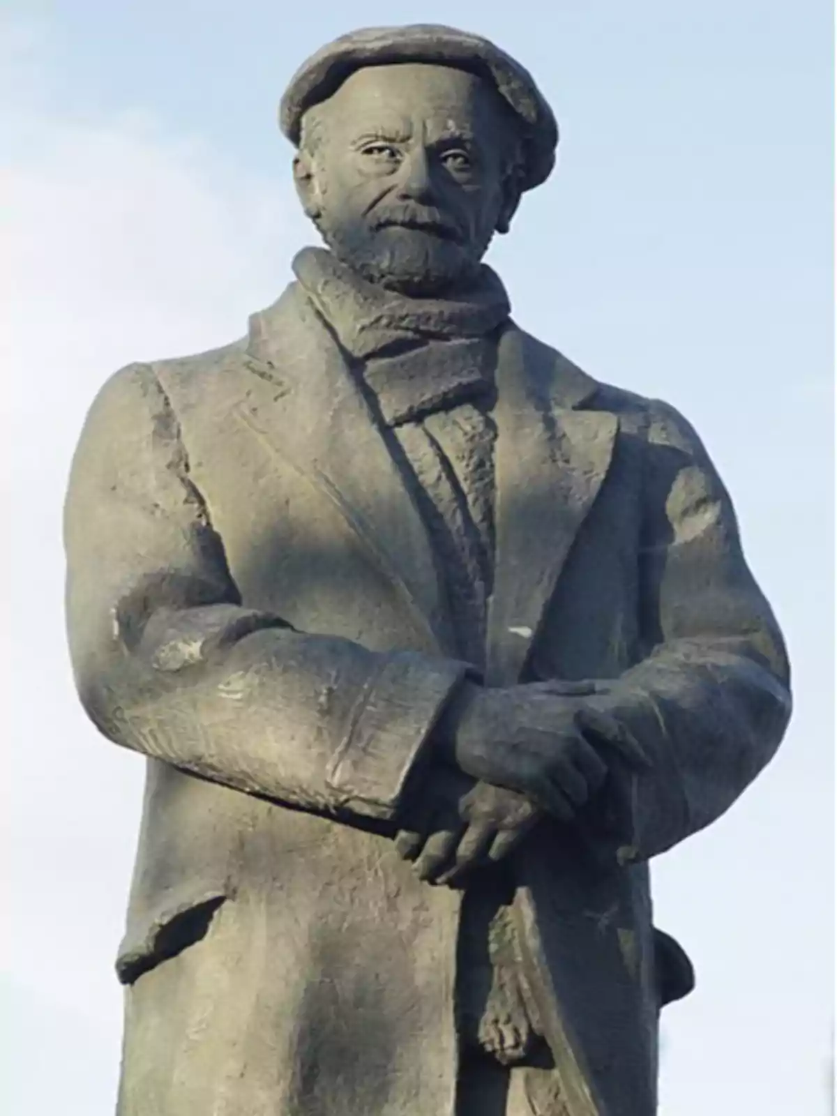 Estatua de un hombre con abrigo, bufanda y gorra.