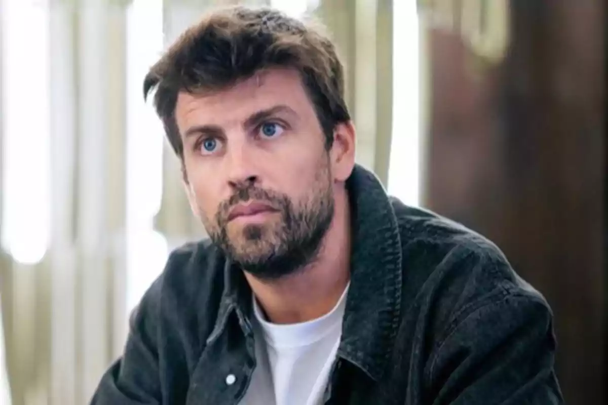 Hombre de cabello castaño y barba con chaqueta oscura y camiseta blanca mirando hacia el frente en un ambiente interior iluminado