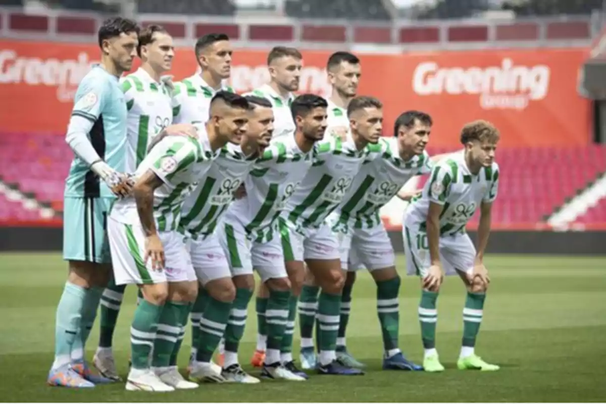 Un equipo de fútbol posando para una foto en el campo antes de un partido, con uniformes blancos y verdes.