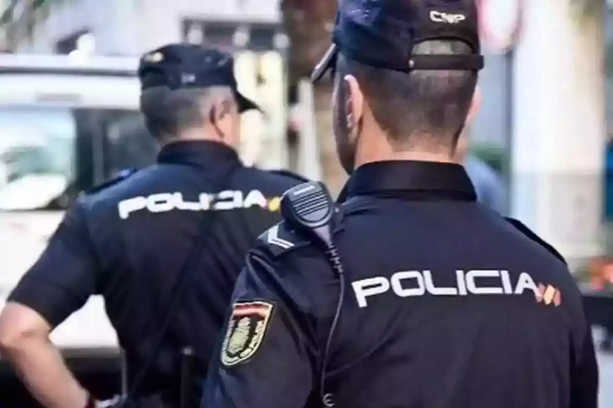 Dos policías de espaldas con uniformes oscuros y gorras en una calle.