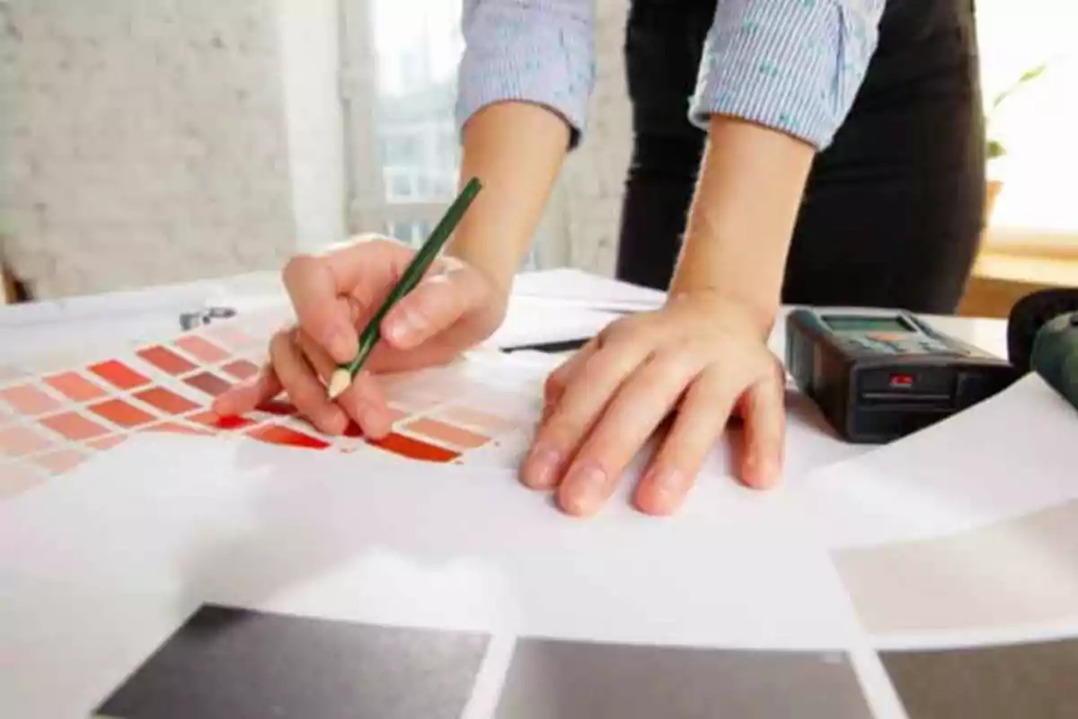 Manos de una persona trabajando con una paleta de colores y un lápiz sobre una mesa.