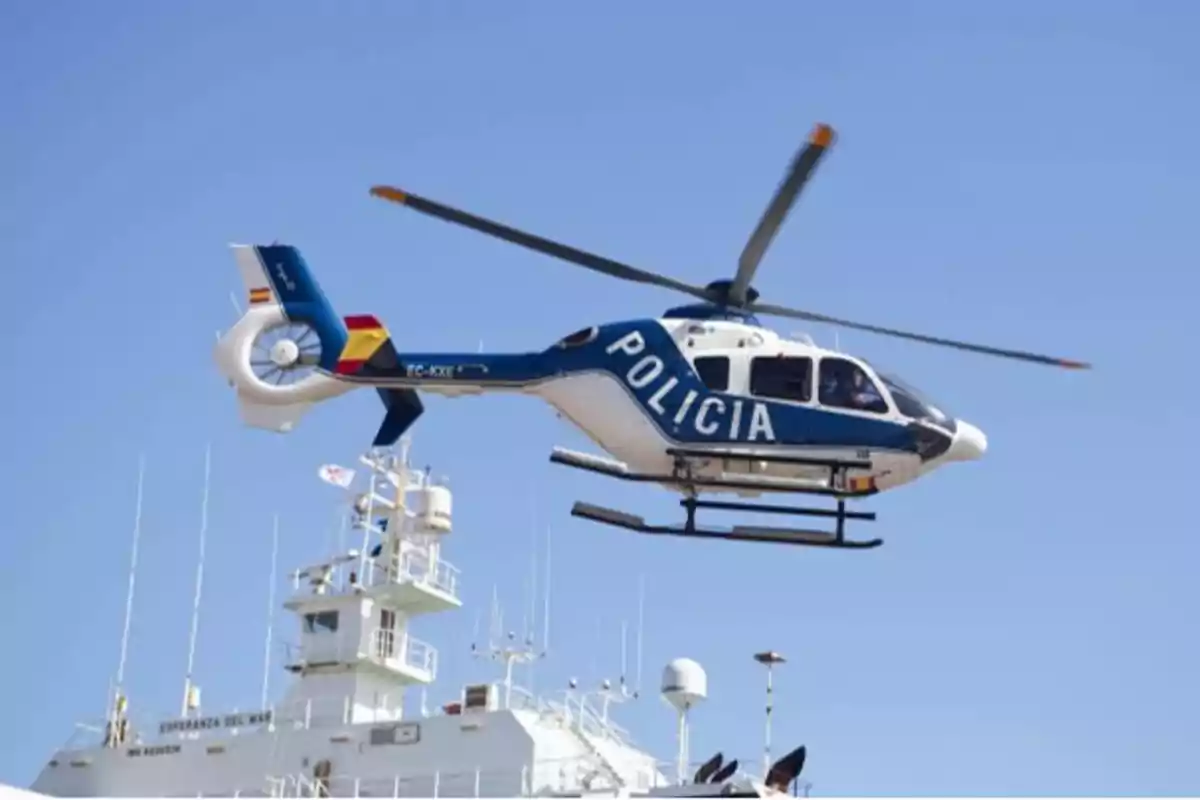 Un helicóptero de la policía volando sobre un barco en un cielo despejado.