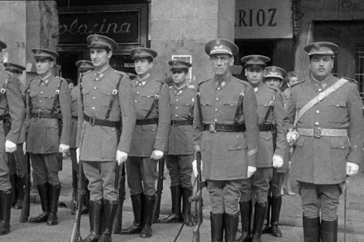 Un grupo de soldados en uniforme militar posando en formación frente a un edificio.