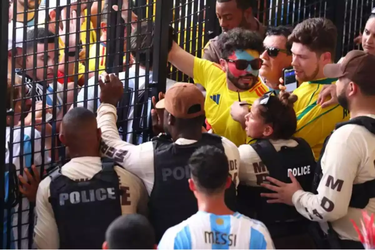Aficionados de fútbol discuten con la policía a través de una reja durante un evento deportivo.