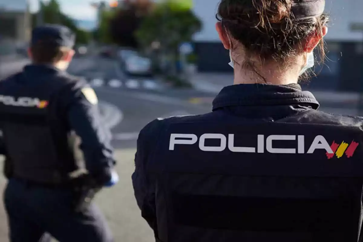 Dos agentes de policía de espaldas en una calle urbana.