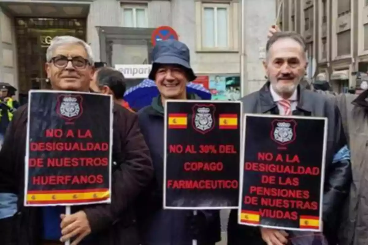 Tres hombres sostienen carteles de protesta que dicen 