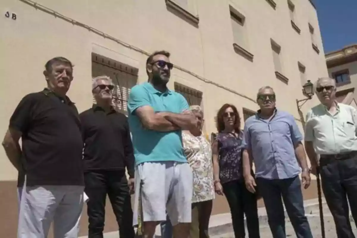 Un grupo de personas posando frente a un edificio bajo el sol.