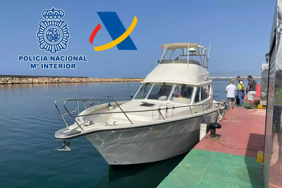 Un barco atracado en un muelle con varias personas a su lado y los logotipos de la Policía Nacional y la Agencia Tributaria en la parte superior izquierda.