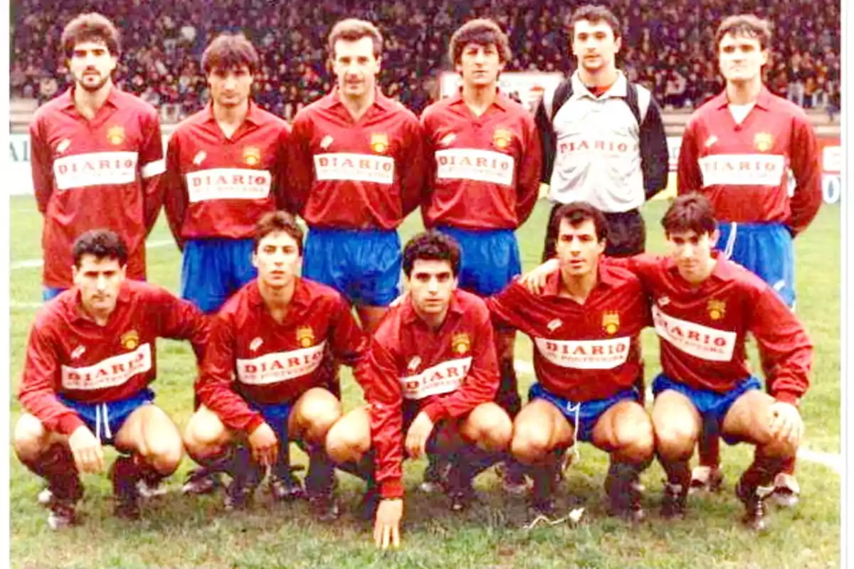 Un equipo de fútbol posando en el campo con uniformes rojos y pantalones cortos azules.