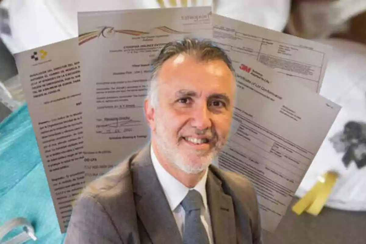 Un hombre con traje y corbata sonríe frente a varios documentos oficiales.
