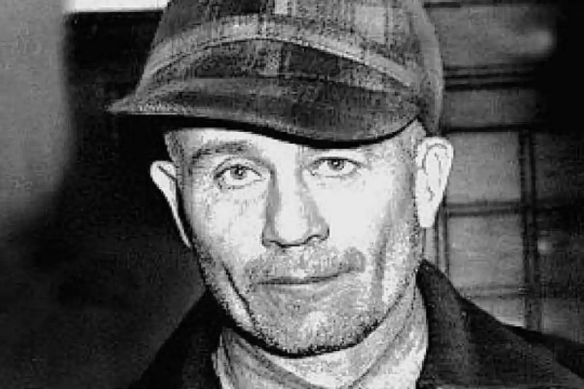Un hombre con gorra y barba incipiente mirando a la cámara en una fotografía en blanco y negro.