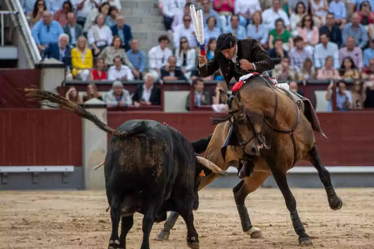 Un torero montado a caballo enfrenta a un toro en una plaza de toros llena de espectadores.