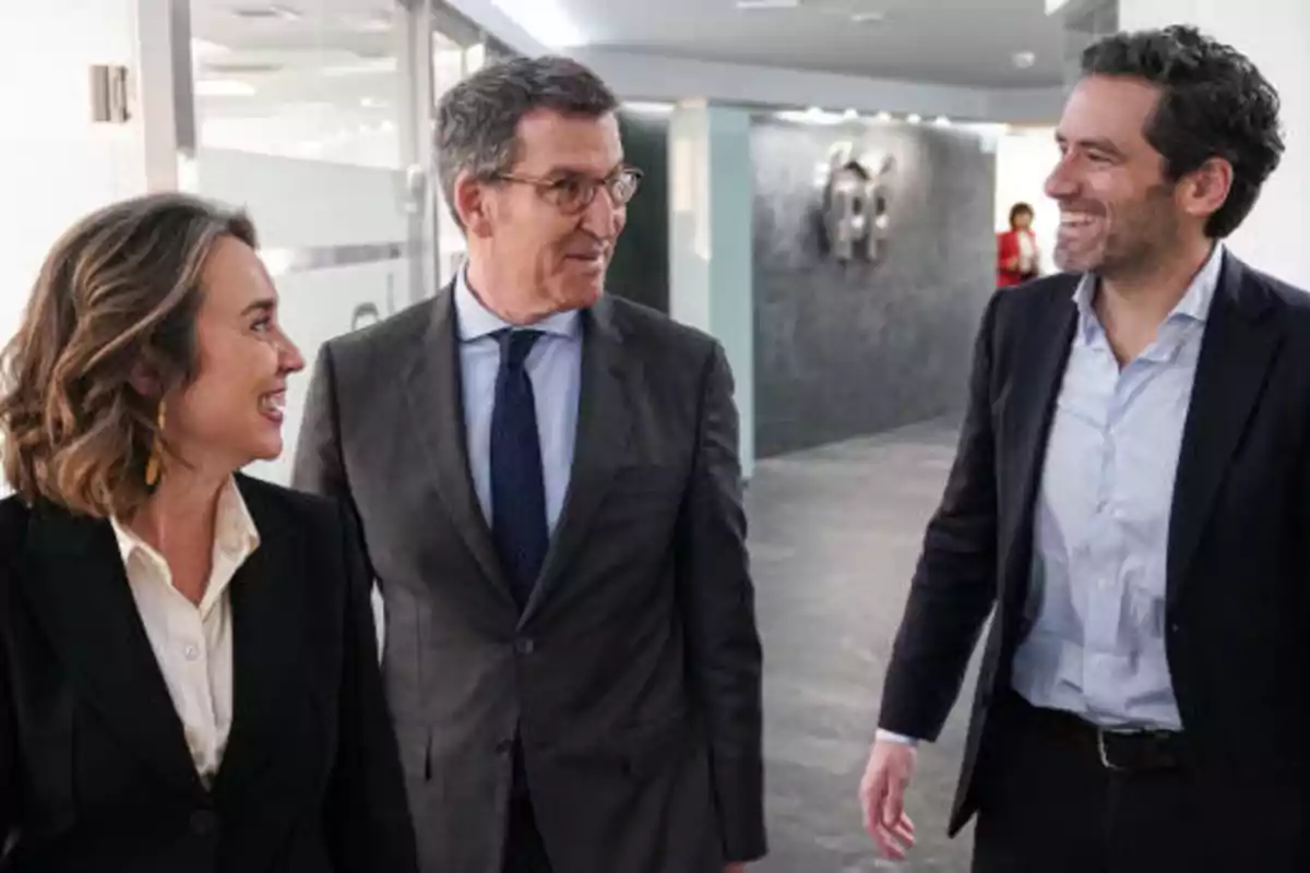 Tres personas vestidas de traje conversando y sonriendo mientras caminan por un pasillo de oficina.
