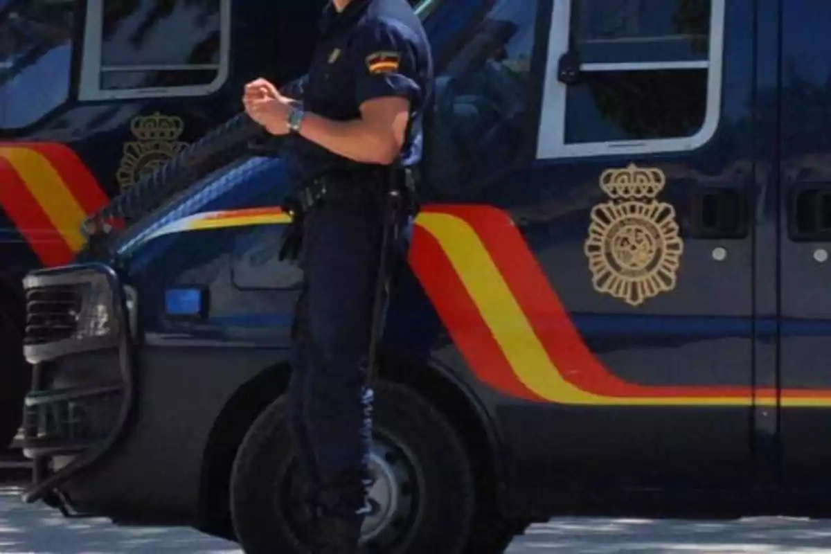 Policía de pie junto a una furgoneta con los colores y emblemas de la Policía Nacional de España.
