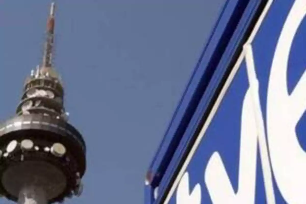Torre de telecomunicaciones junto a un cartel azul con letras blancas.