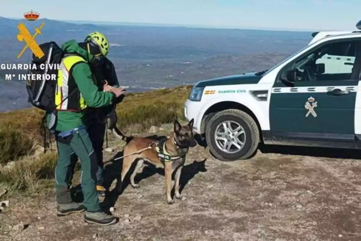 Dos miembros de la Guardia Civil con equipo de montaña y un perro de rescate junto a un vehículo oficial en un entorno natural.