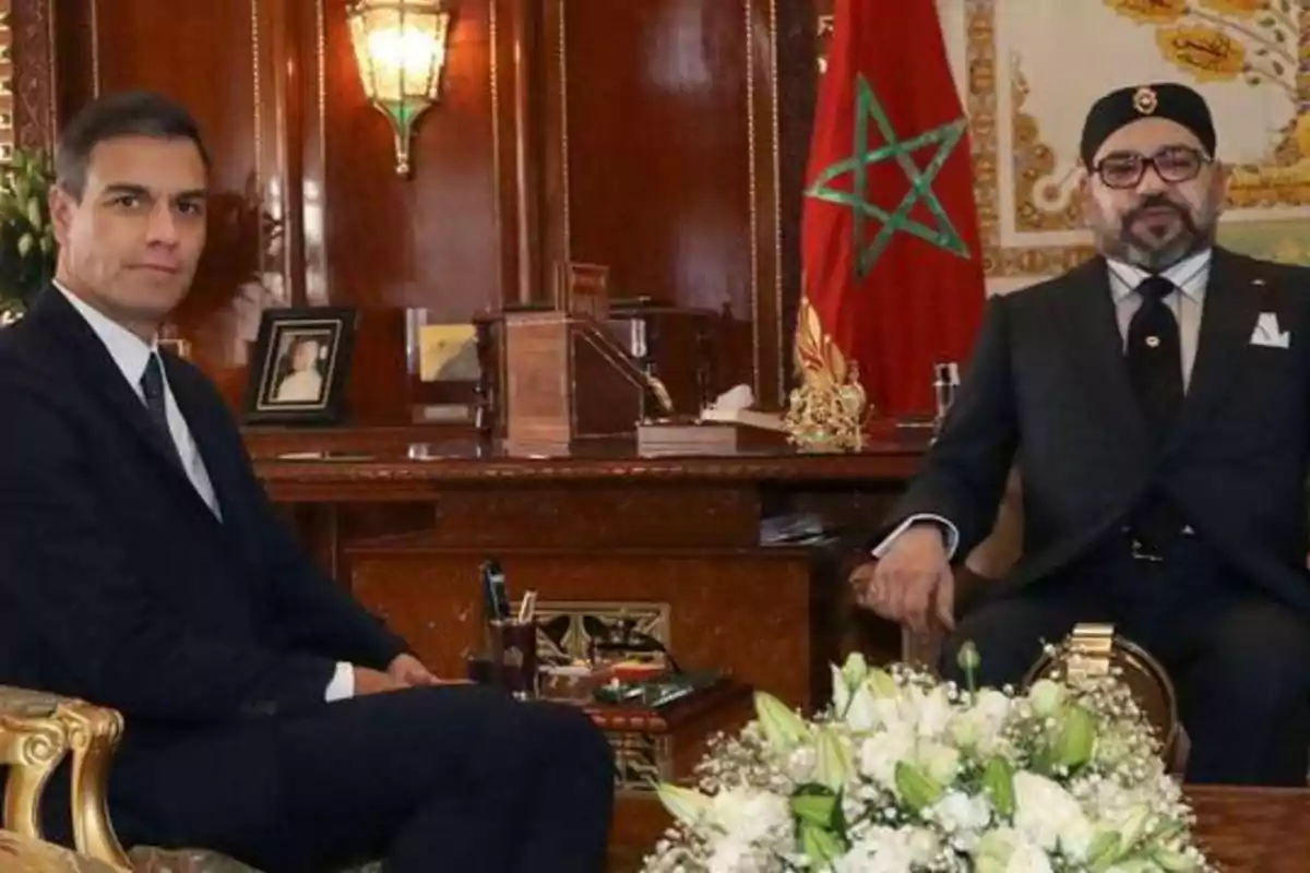 Dos hombres sentados en una oficina elegante con una bandera de Marruecos en el fondo.