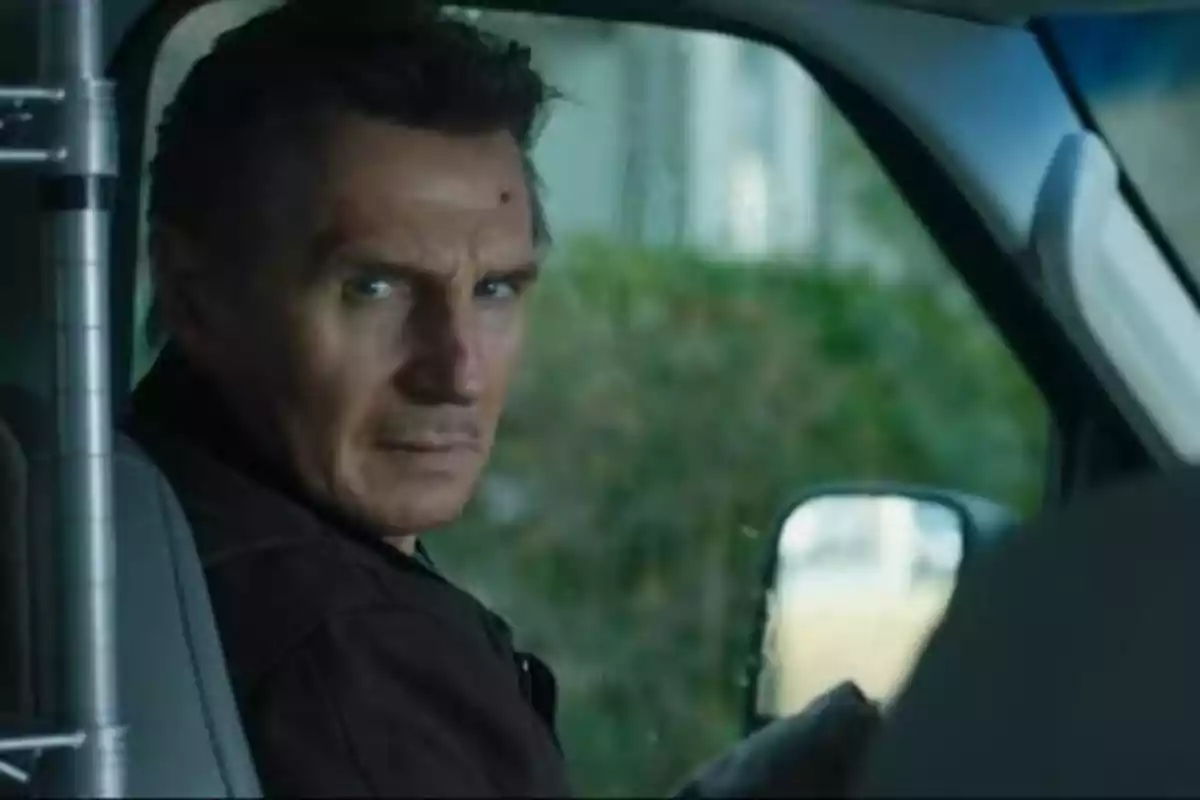 Un hombre con expresión seria sentado en el asiento del conductor de un vehículo, mirando hacia atrás.