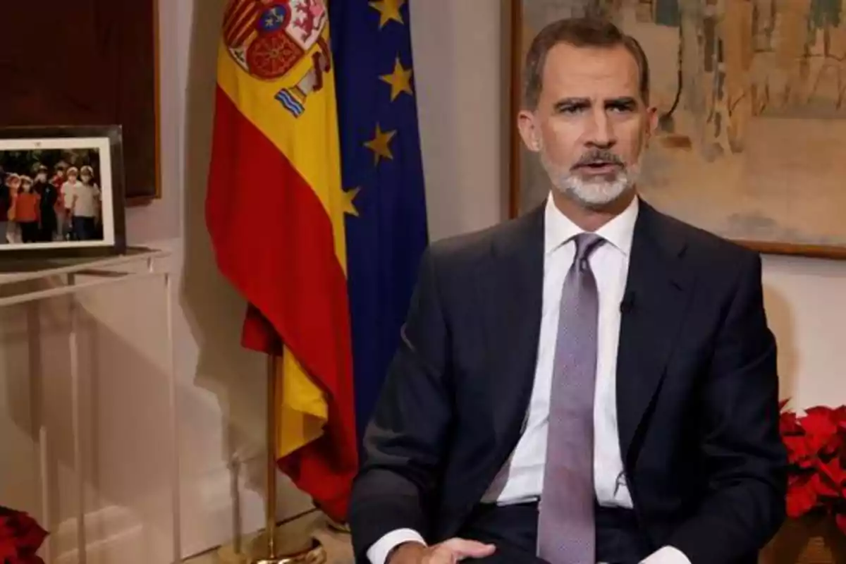 Hombre con traje y corbata sentado frente a las banderas de España y la Unión Europea.