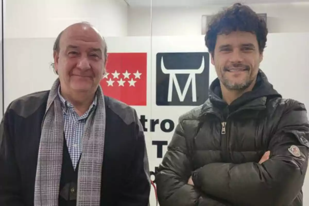 Dos hombres posando frente a un cartel con el logo de la Comunidad de Madrid y el logo de Metro de Madrid.