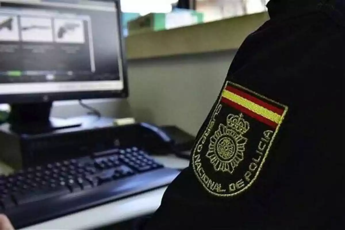 Un agente de policía trabajando en una computadora con el emblema de la Policía Nacional visible en su uniforme.