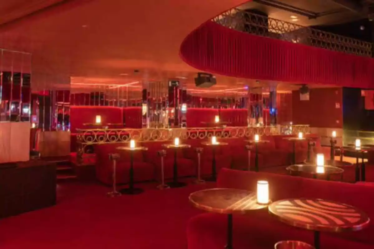 Un club nocturno con decoración en tonos rojos, mesas redondas y luces tenues.