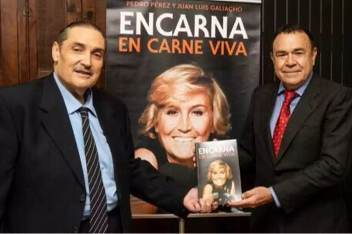 Dos hombres posan junto a un cartel y un libro titulado "Encarna en carne viva" que muestra la imagen de una mujer rubia sonriente.