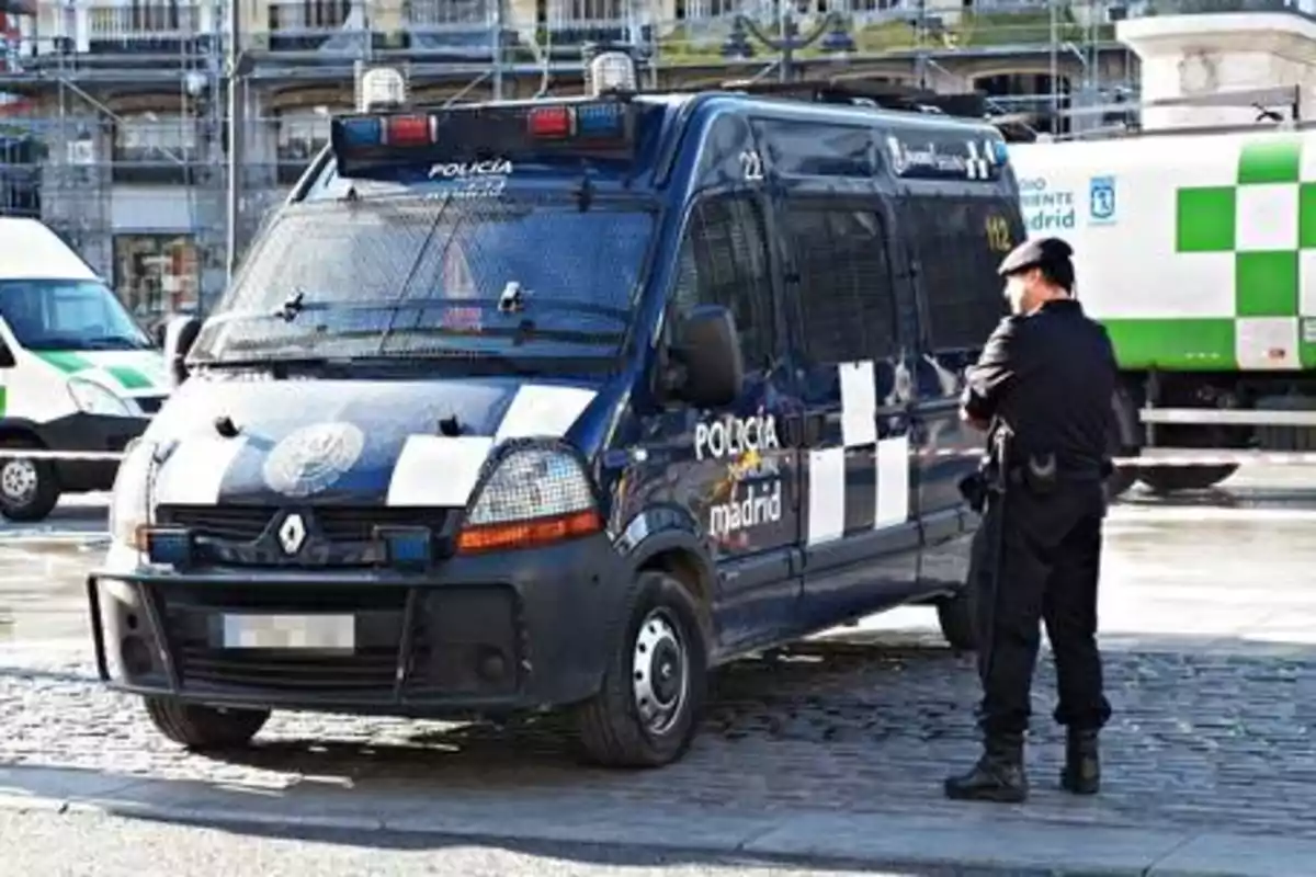 Un vehículo de la policía de Madrid estacionado en una calle con un agente de pie al lado.