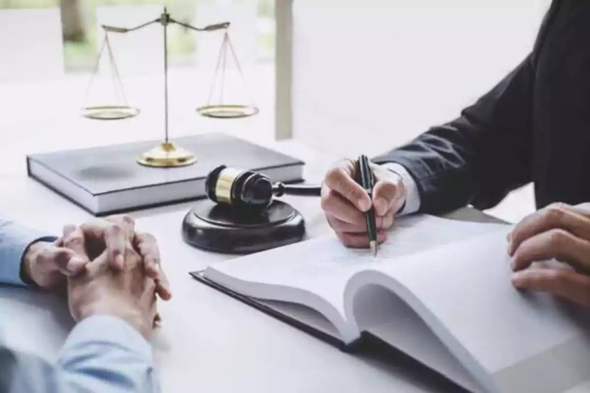 Dos personas en una reunión legal con un mazo, una balanza y documentos sobre la mesa.