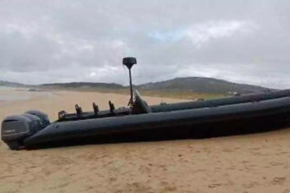 Una lancha inflable negra varada en la playa con colinas al fondo.