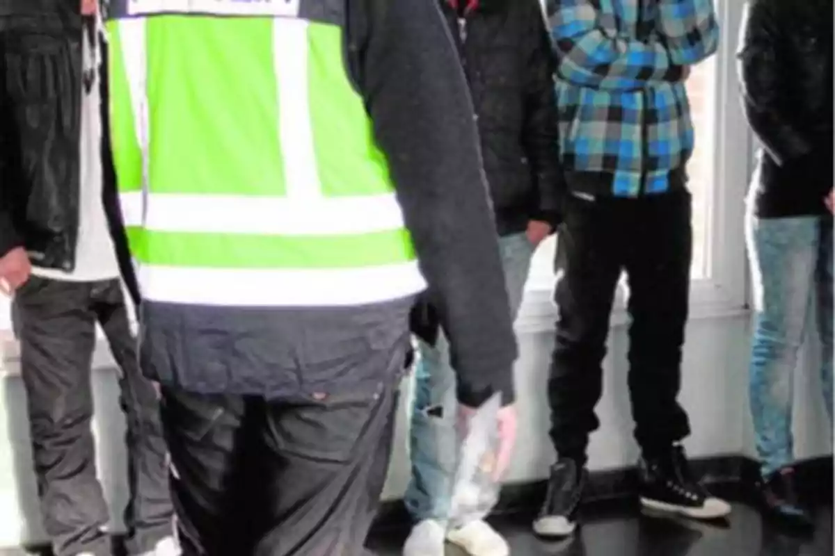 Un grupo de personas de pie junto a un oficial con chaleco reflectante verde.