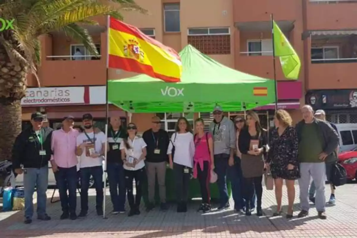 Un grupo de personas posando frente a una carpa verde con el logo de Vox y una bandera de España.