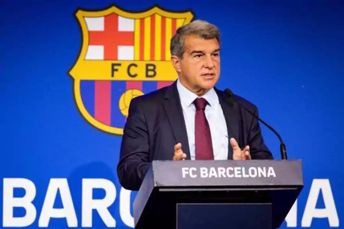 Un hombre en traje y corbata habla en un podio con el logo del FC Barcelona de fondo.