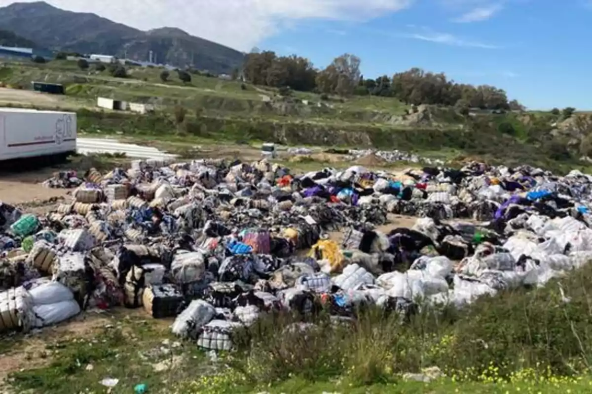 Montones de ropa y textiles desechados en un terreno al aire libre con montañas y vegetación en el fondo.