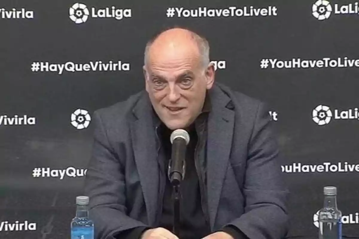 Un hombre en una conferencia de prensa con un fondo que tiene los logotipos de LaLiga y los hashtags #HayQueVivirla y #YouHaveToLiveIt.
