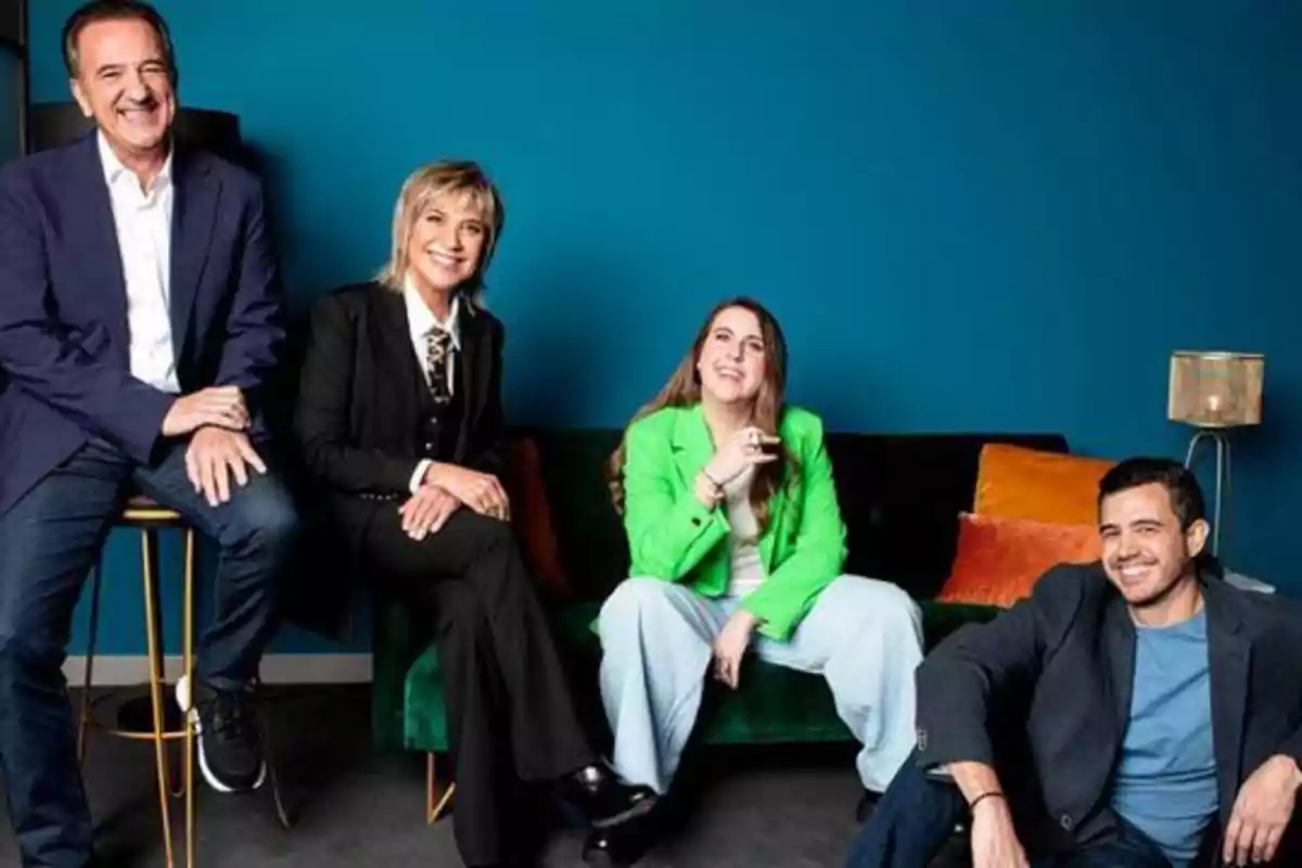 Cuatro personas posan sonrientes en una sala con una pared azul de fondo, dos de ellas están sentadas en un sofá verde y las otras dos en taburetes.