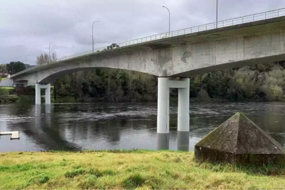 Un puente de concreto sobre un río con un paisaje de árboles y césped en primer plano.