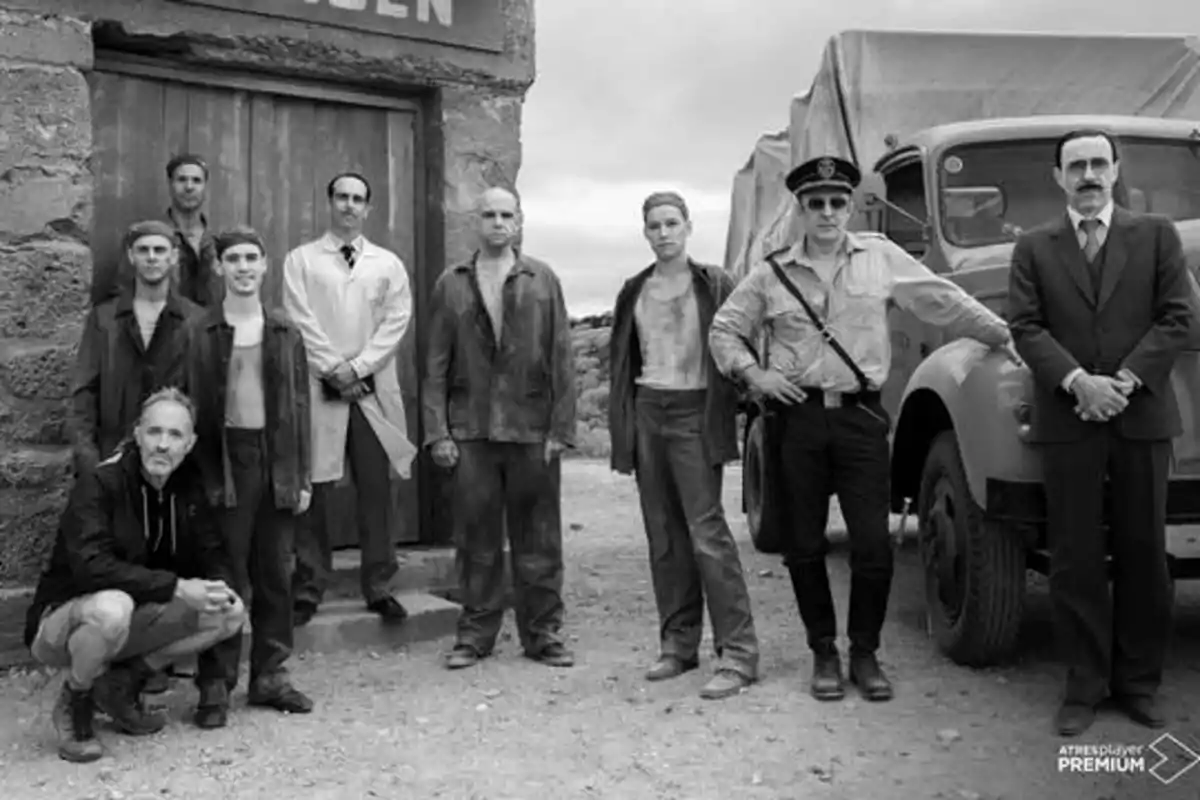 Un grupo de personas posando frente a un edificio de piedra y un camión, algunas vestidas con ropa de trabajo y otras con uniformes.