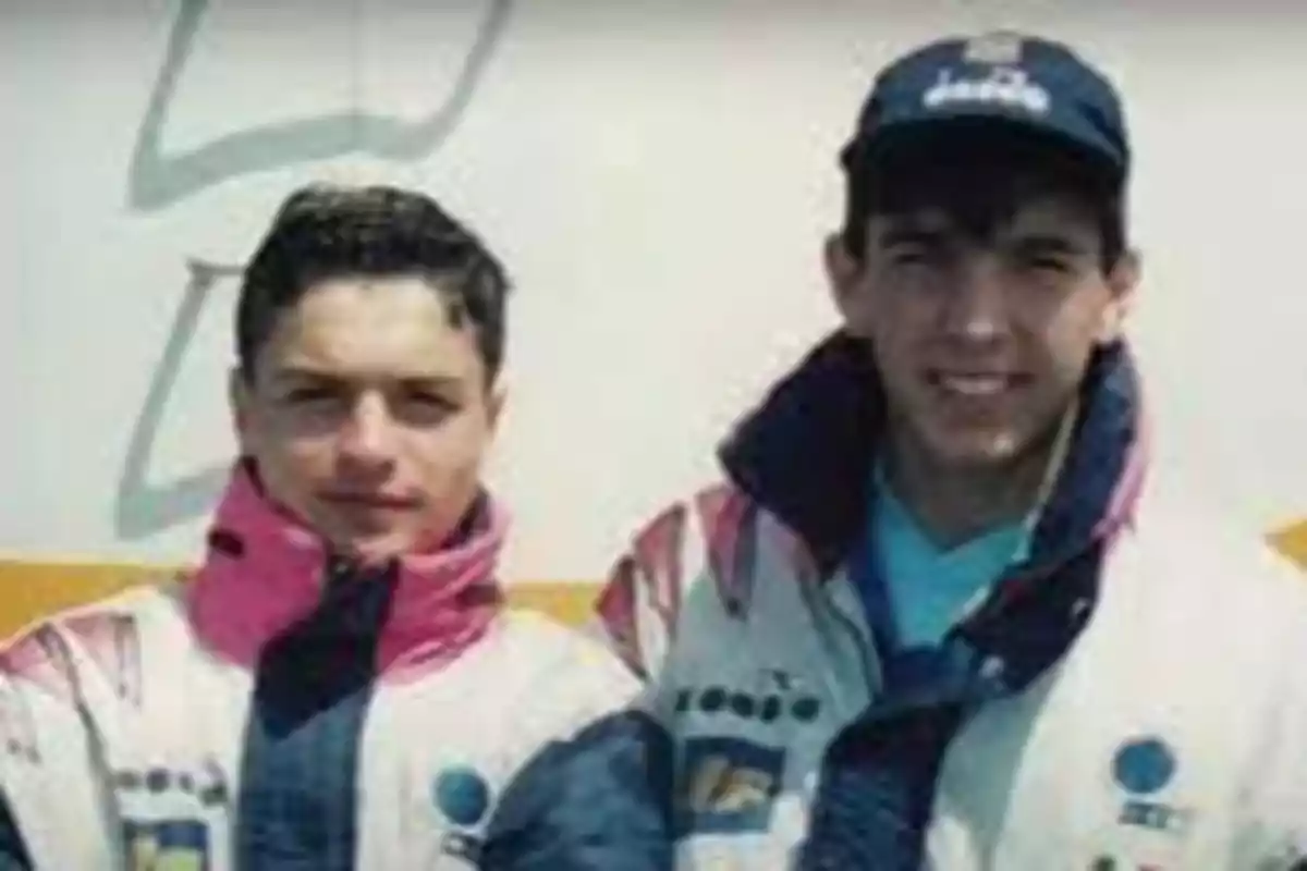 Dos jóvenes con chaquetas deportivas posan para una foto, uno de ellos lleva una gorra azul.