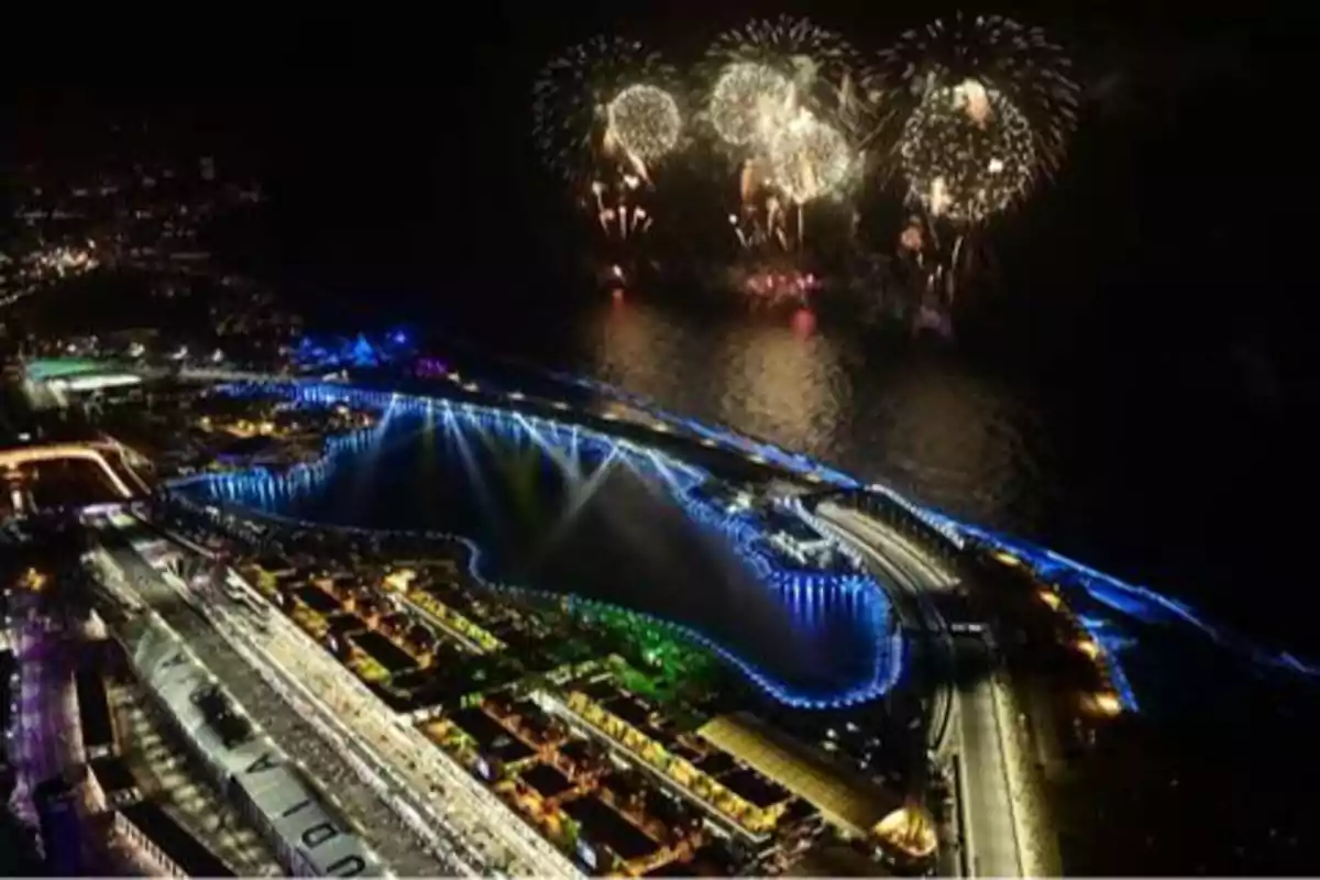 Vista nocturna de un circuito de carreras iluminado con fuegos artificiales en el cielo.